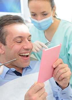 Dentist looking over shoulder of man admiring results of treatment in mirror