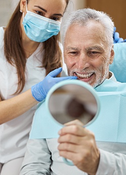 An older man admiring his new dental implant with a hand mirror