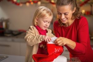 A mother helping her daughter pull treats out of a Christmas stocking.