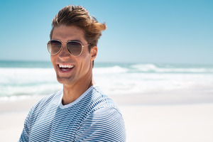 Man with sunglasses standing on beach and laughing