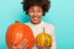 Woman in white sweater smiling and holding 2 pumpkins
