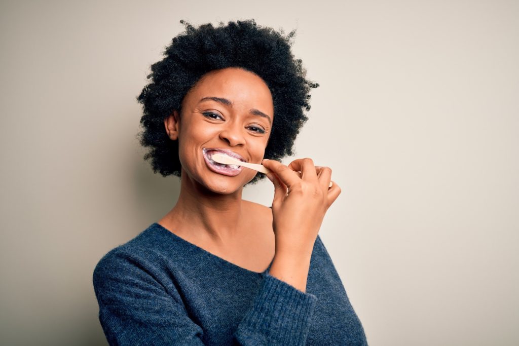 Woman in blue sweater smiling while brushing her teeth